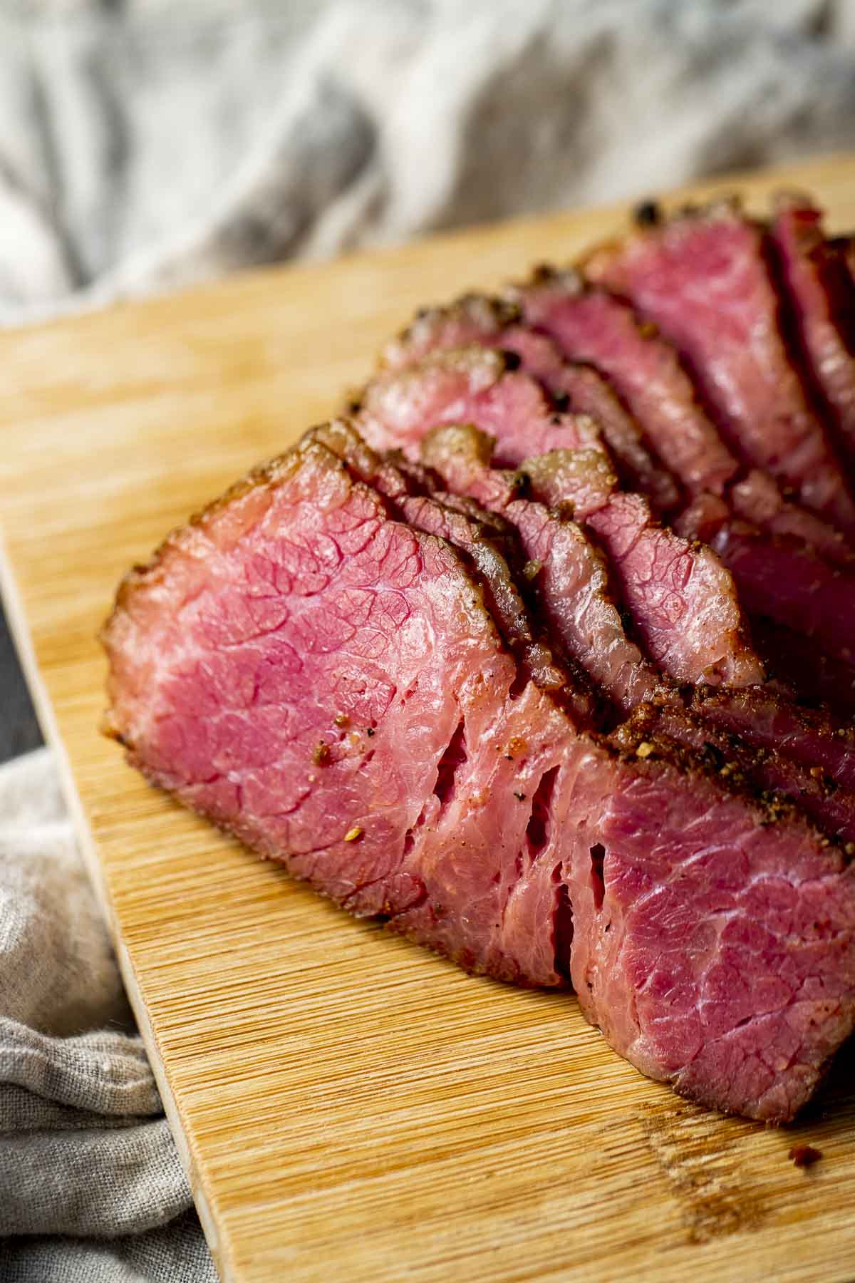 Close up view of thinly sliced pastrami on a wooden board.