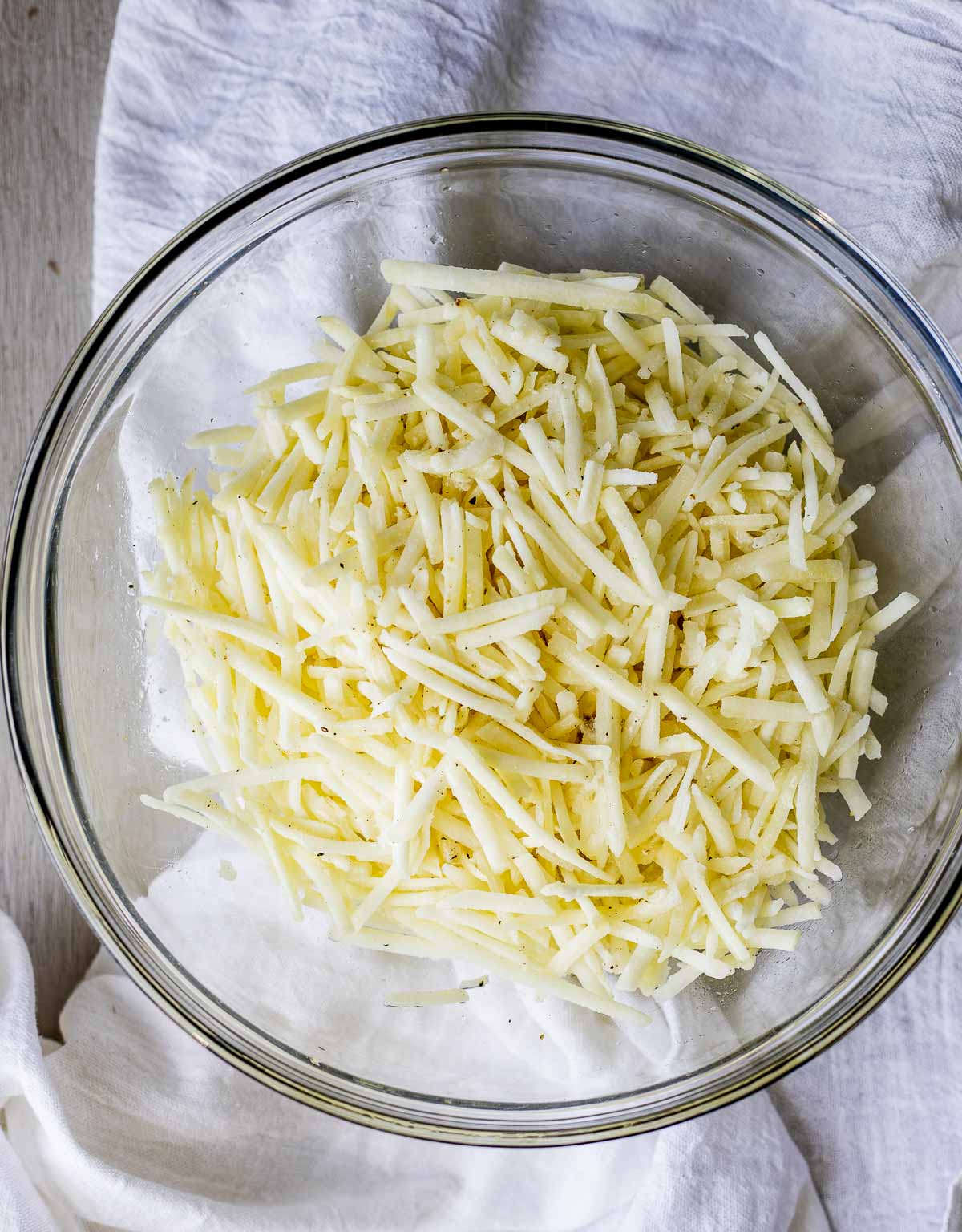 Shredded frozen hash browns in a glass bowl.