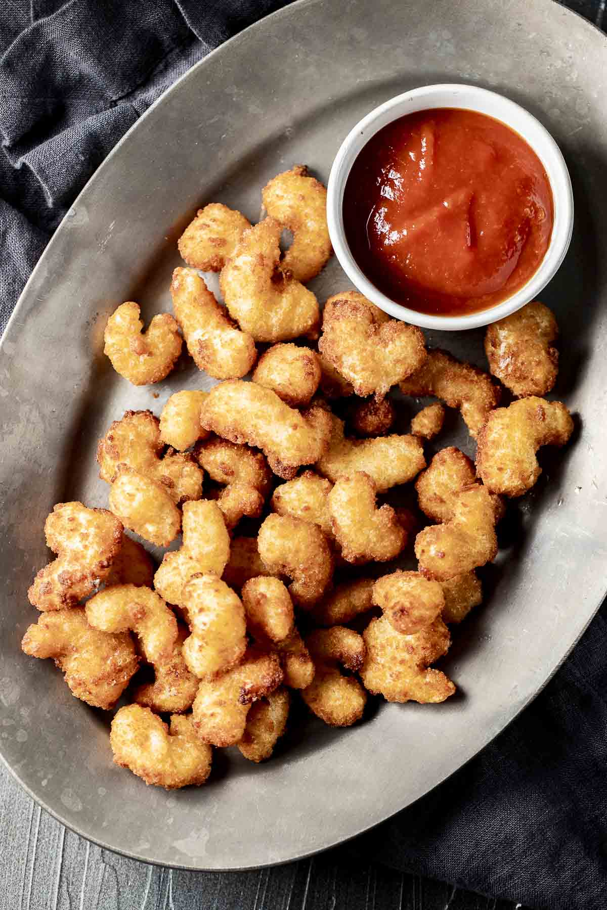 Overhead view of air fryer popcorn shrimp on a grey platter with a small bowl of cocktail sauce.