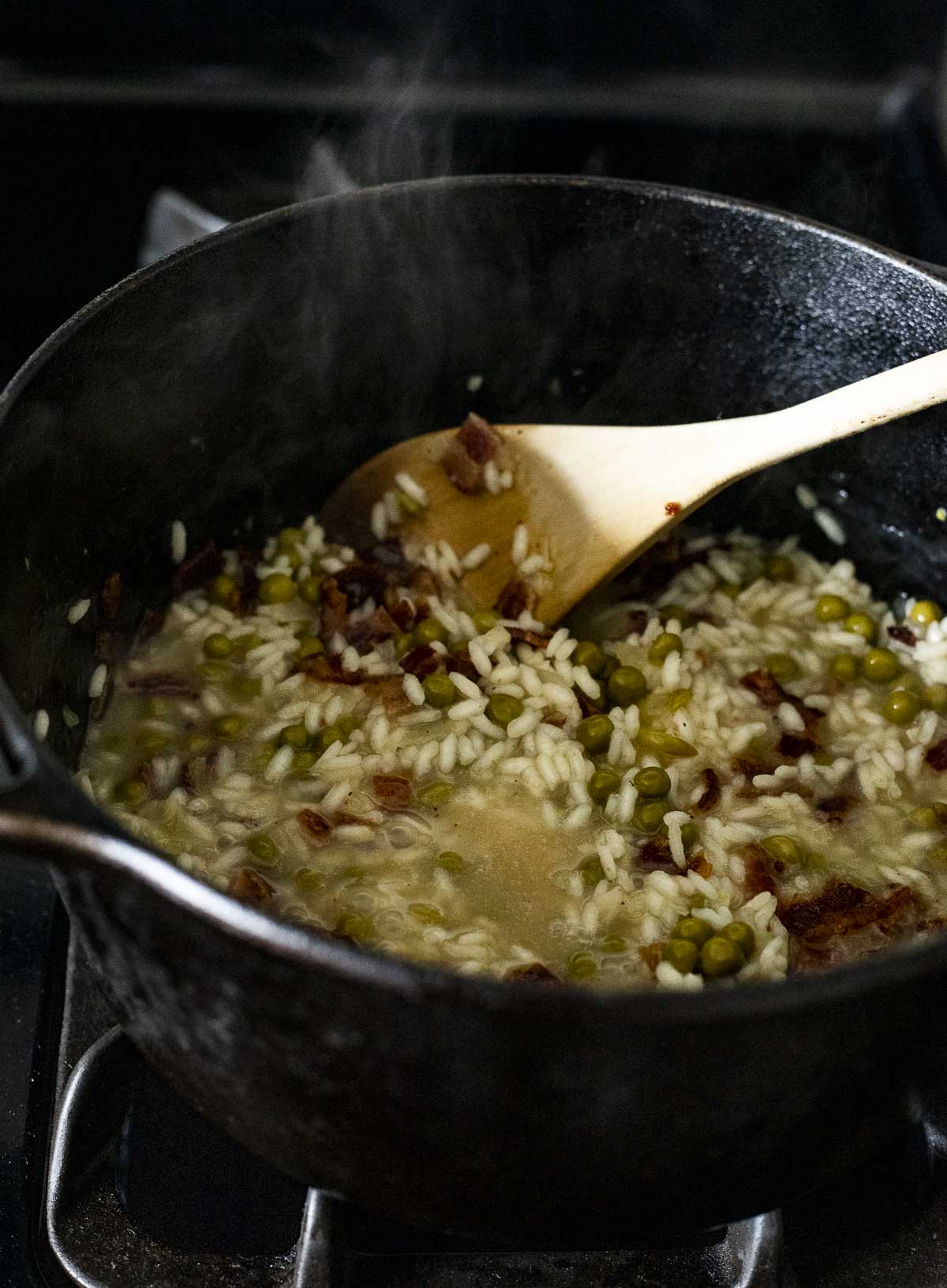 Risotto being stirred around in a Dutch oven with a wooden spoon.