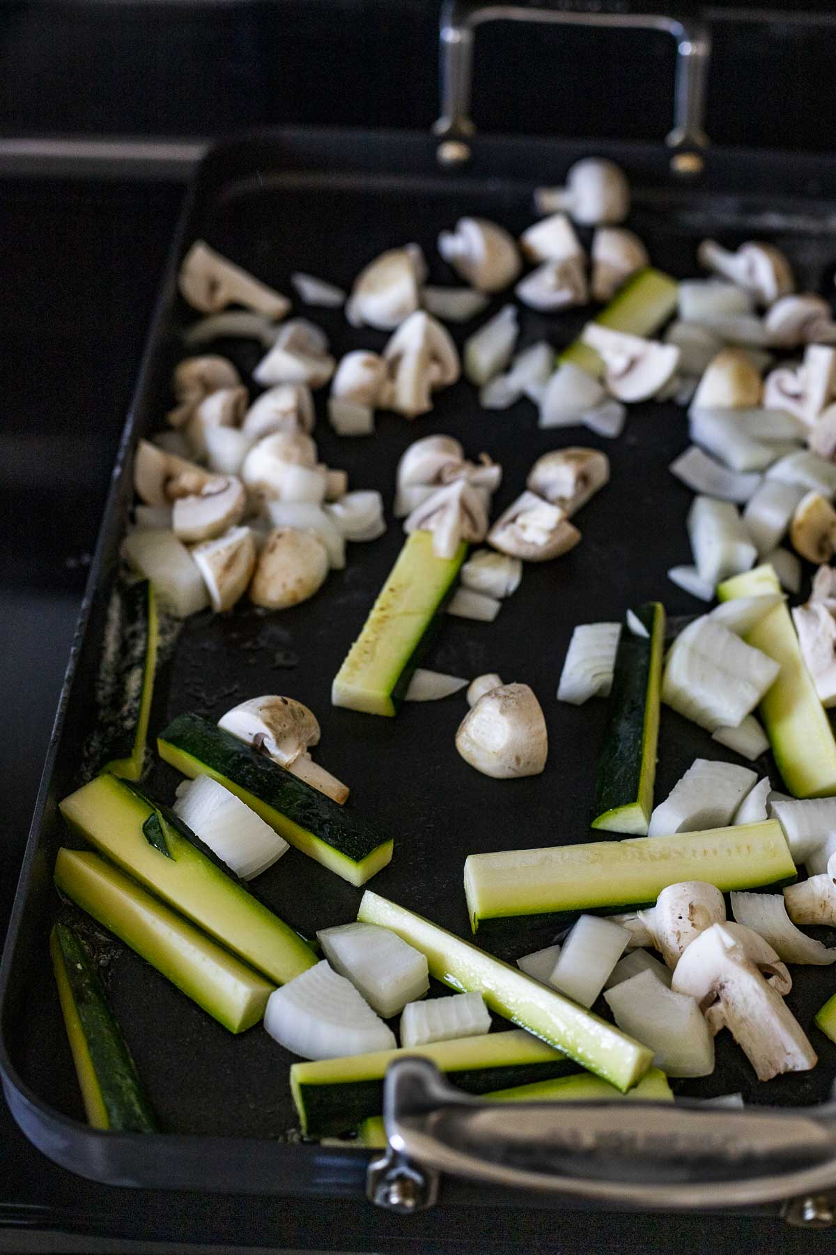 Zucchini, mushrooms and onions cooking on a griddle.
