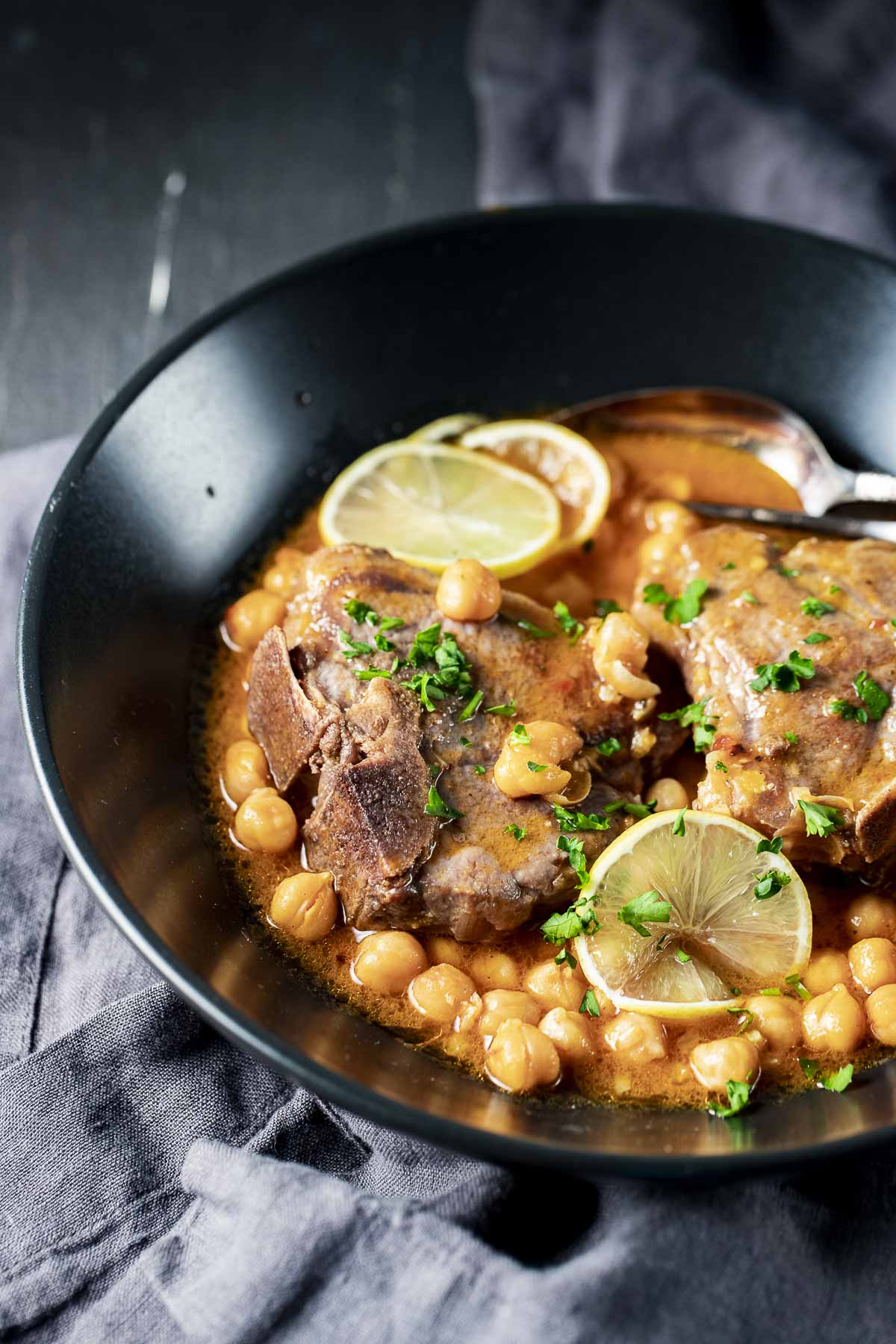 Lamb chops served in a bowl with chickpeas and lemon slices and herbs on top.