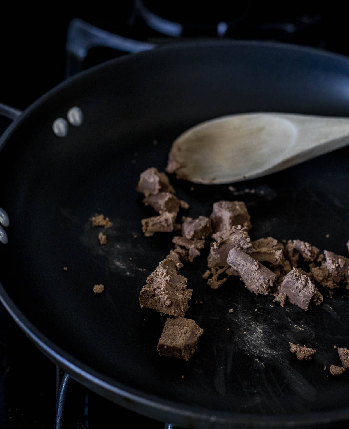 Dried shrimp paste broken into pieces by a wooden spoon in a skillet.