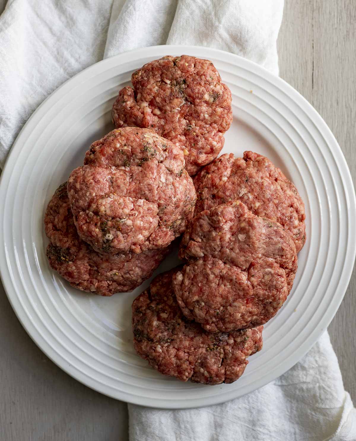 Raw ground beef burger patties on a white plate.