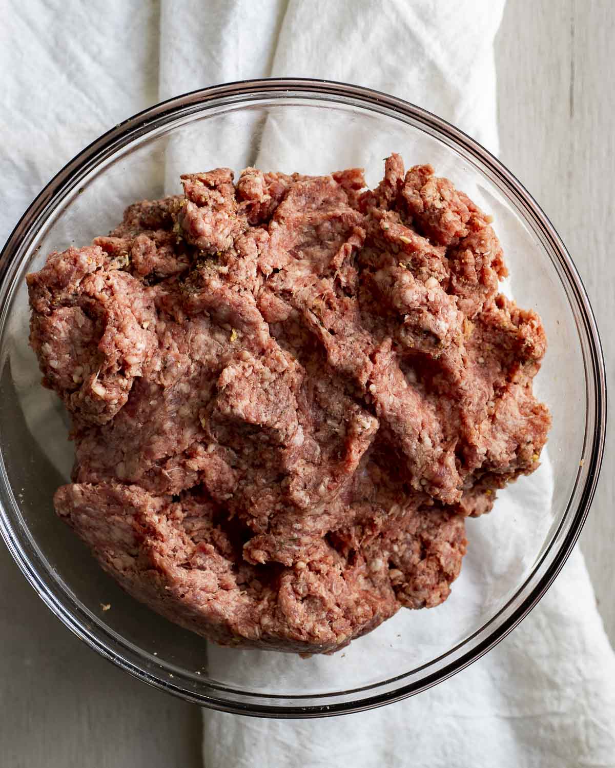Ground beef burger mixture in a glass bowl.