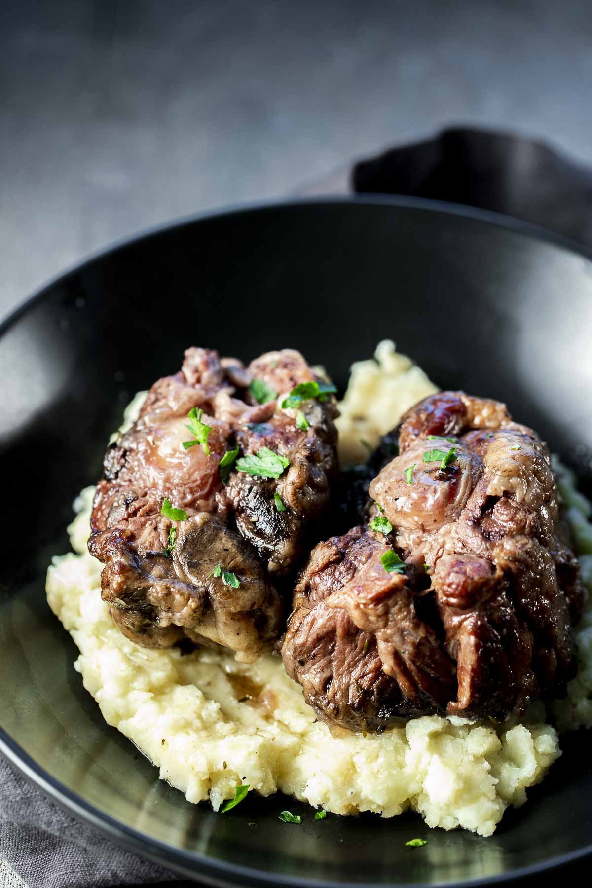 Side view of two pieces of oxtail served on top of mashed potatoes.