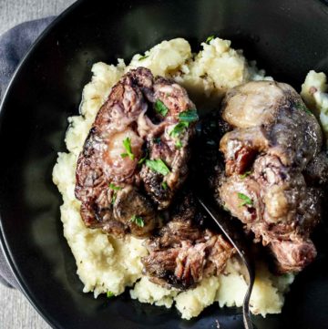 Oxtails served over mashed potatoes in a black bowl.
