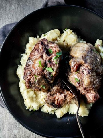 Oxtails served over mashed potatoes in a black bowl.