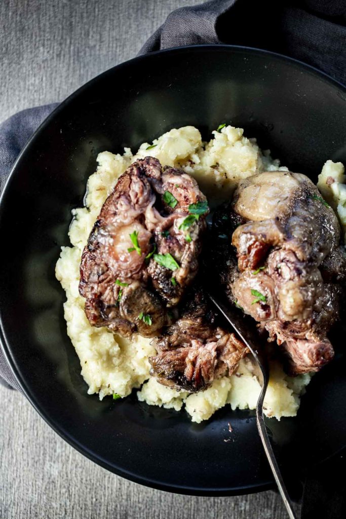 Oxtails served over mashed potatoes in a black bowl.