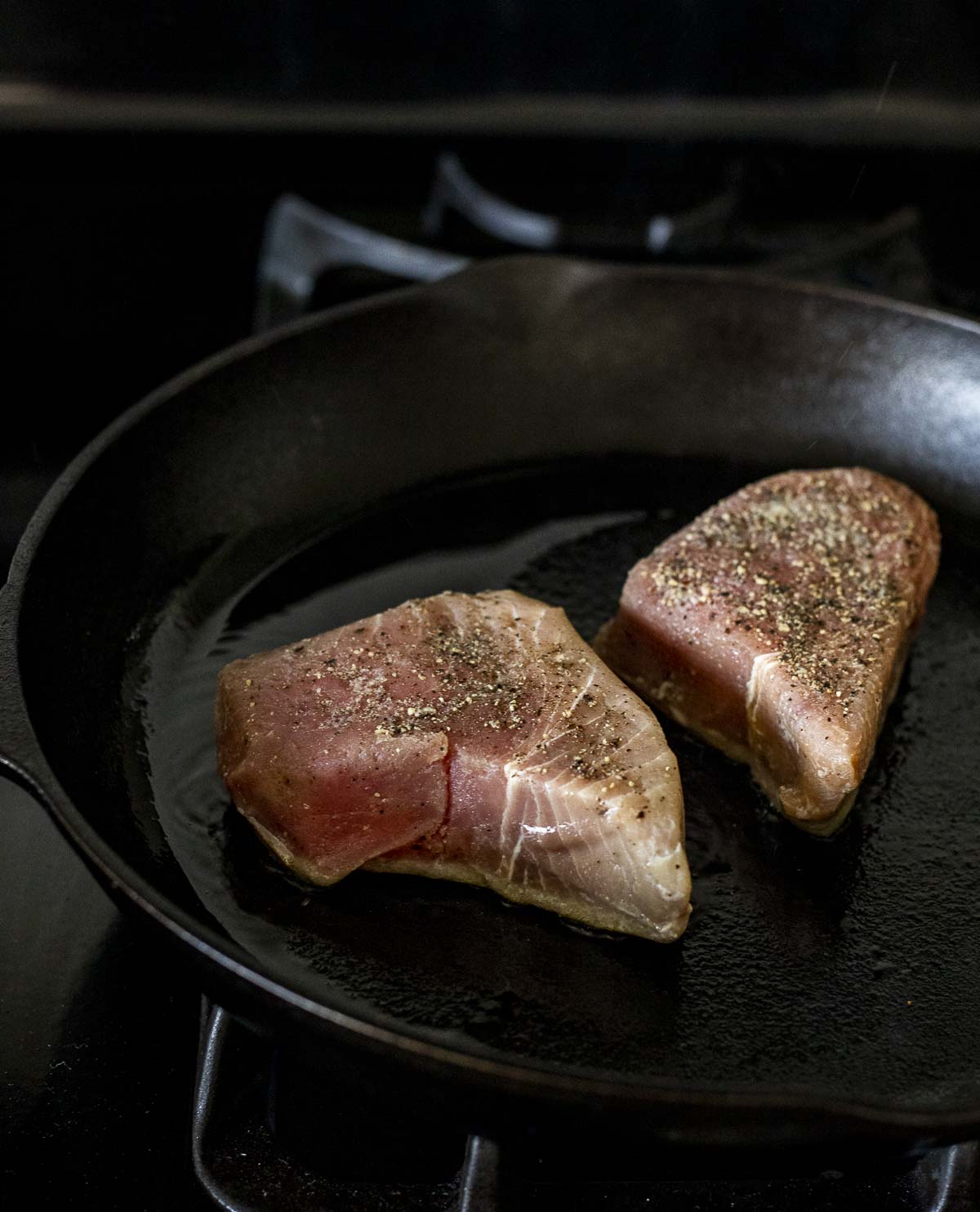 Two tuna steaks being seared in a cast iron skillet.