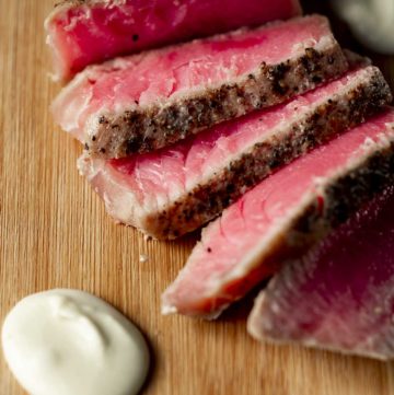 Close up view of sliced tuna on a wooden board with wasabi cream sauce.