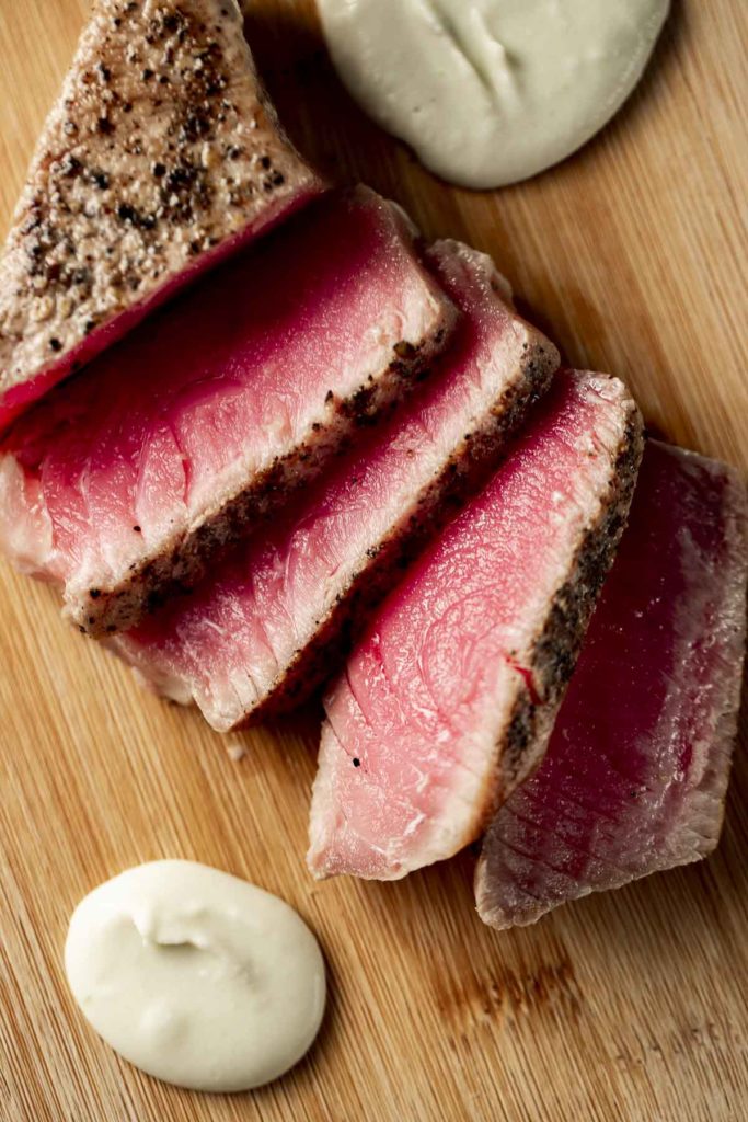 Overhead view of sous vide tuna cut into slices and served on a board with dollops of wasabi cream sauce.