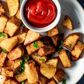 Air fried breakfast potatoes on a plate with a small dish of ketchup.