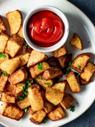 Air fried breakfast potatoes on a plate with a small dish of ketchup.