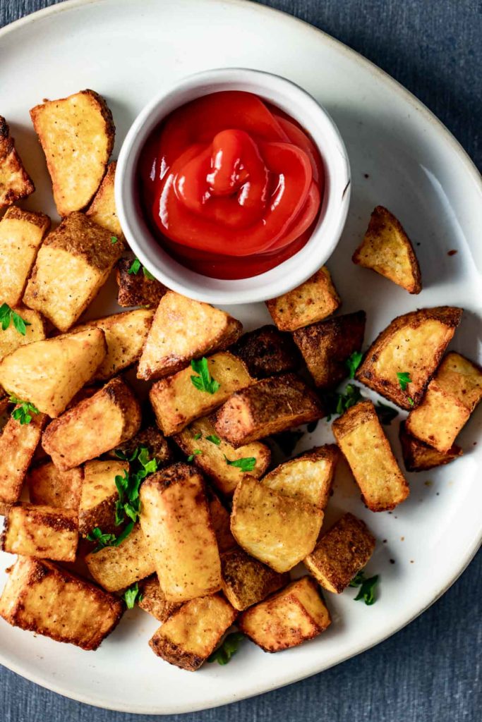 Air fried breakfast potatoes on a plate with a small dish of ketchup.