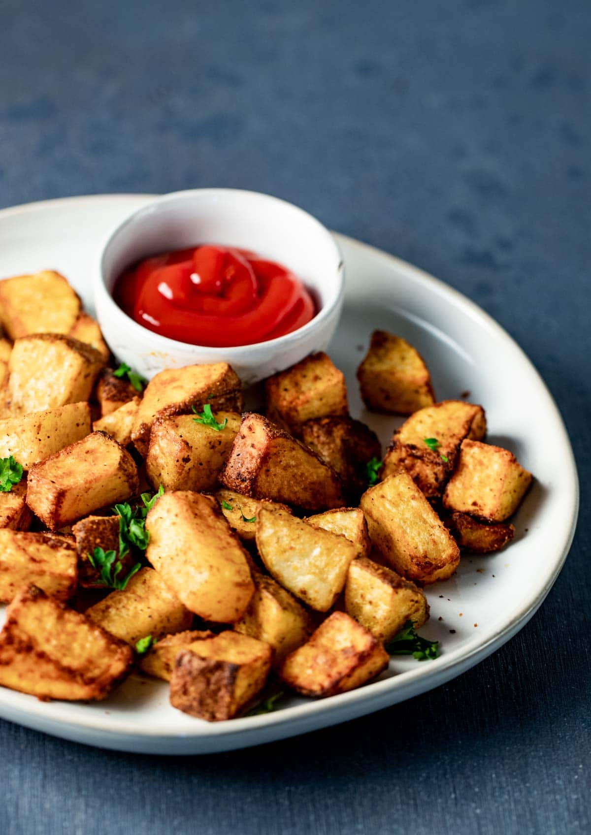 Side view of home fries on a plate with ketchup on the side.