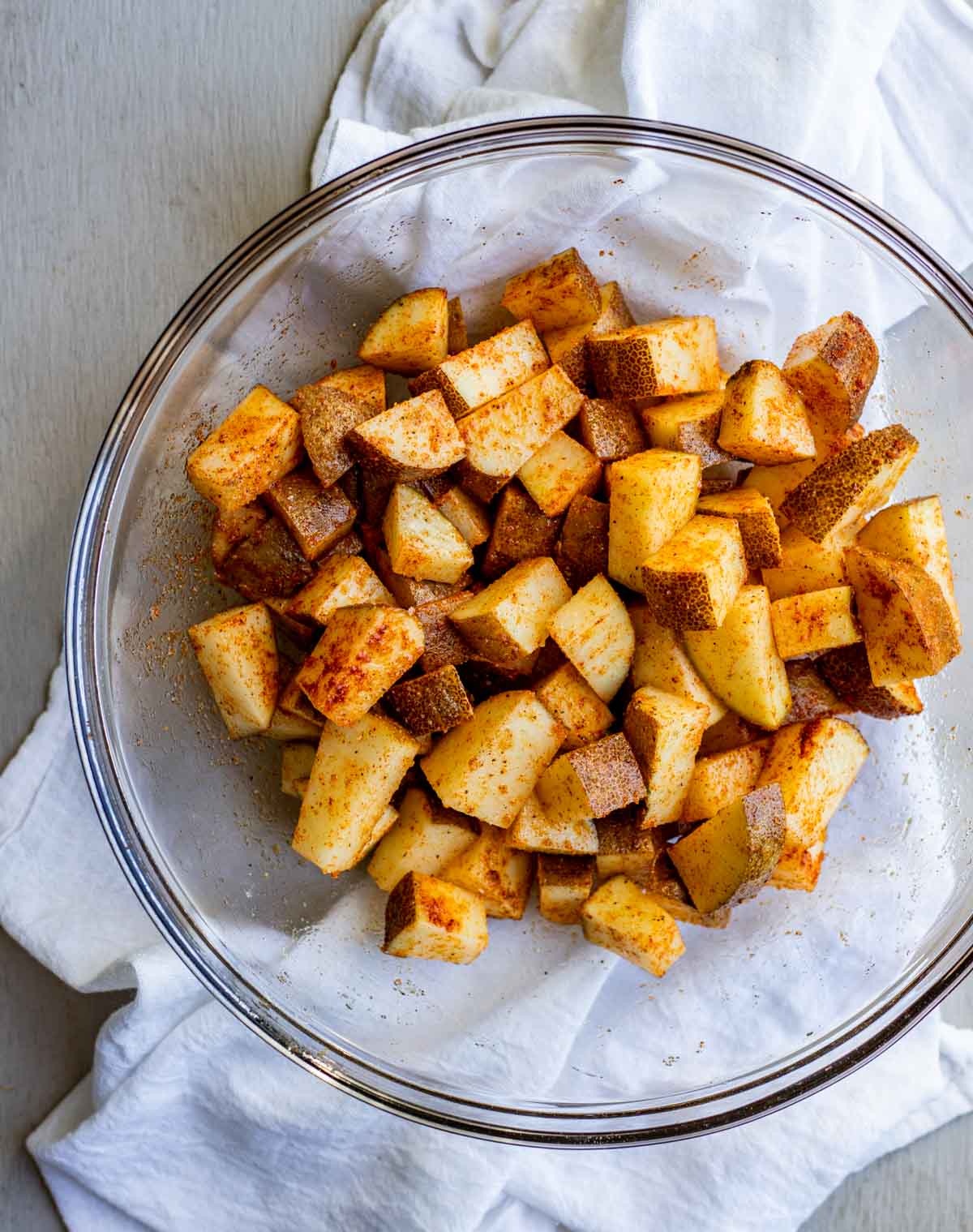 Raw cubed potatoes in a glass bowl and tossed with oil and seasonings.