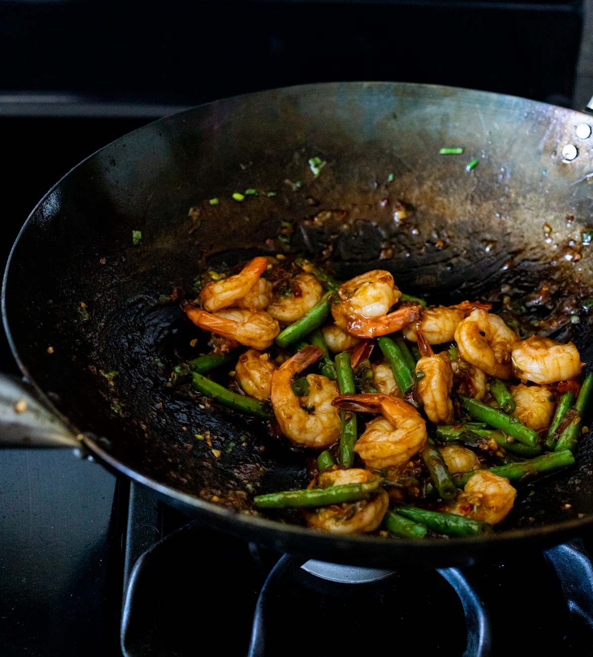 Green beans and shrimp cooking in a wok on the stovetop.