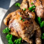 Cornish hens served on a platter with green herbs.