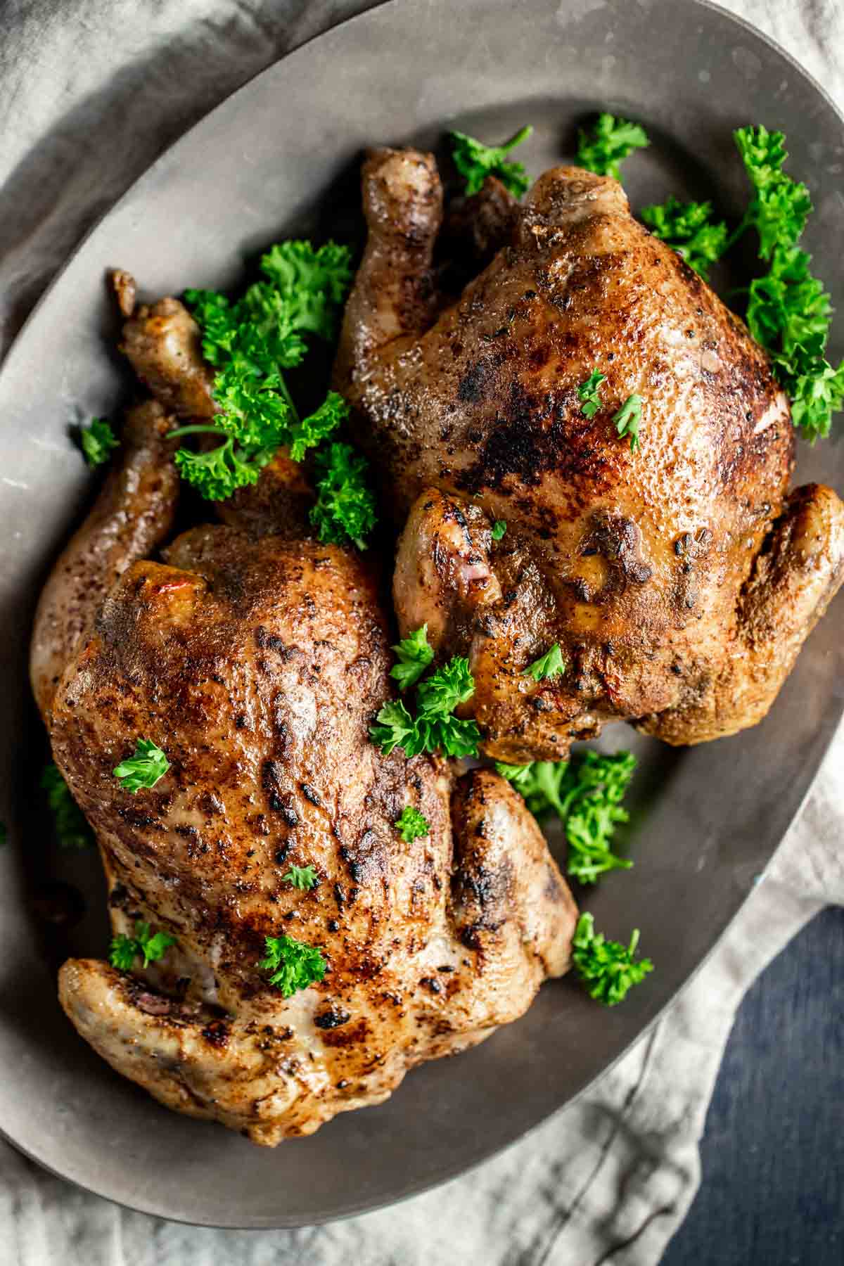 Overhead view of two cornish hens served on a grey platter with fresh herbs.