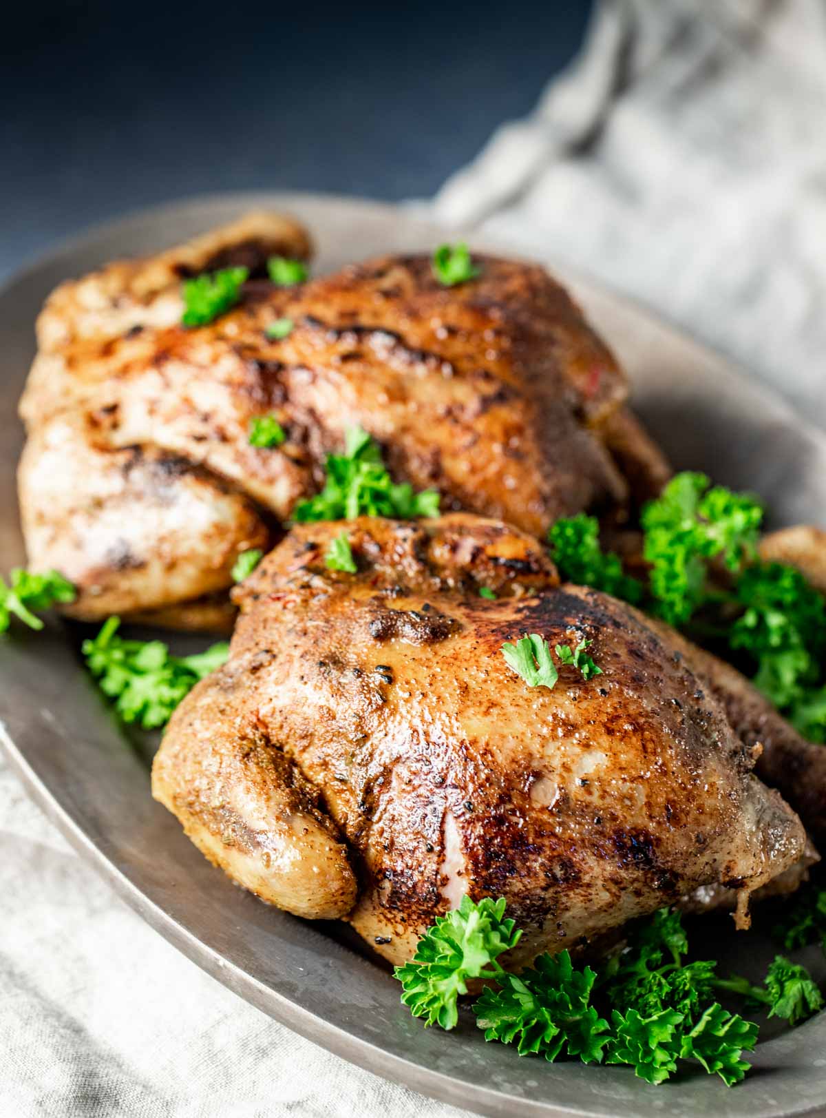Side view of two cornish game hens on a grey platter and garnished with herbs.