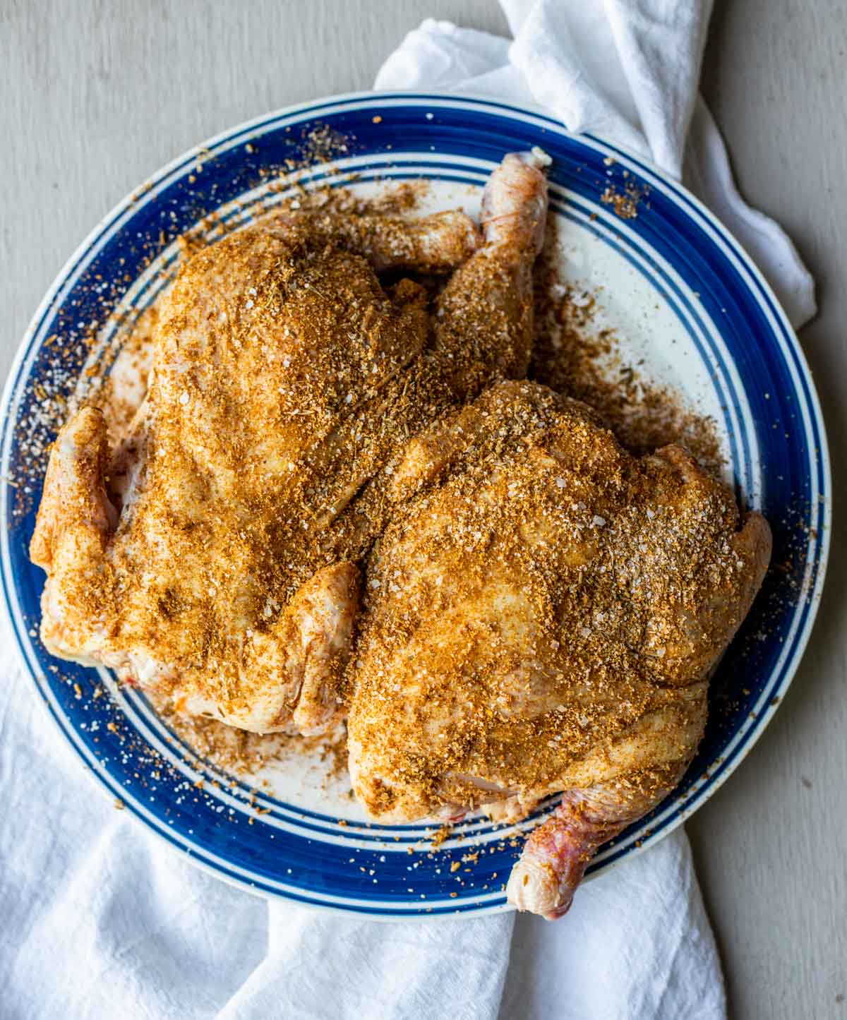 Two cornish hens seasoned with spices and resting on a plate.