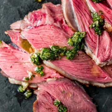 Overhead view of slices of leg of lamb topped with mint chimichurri.