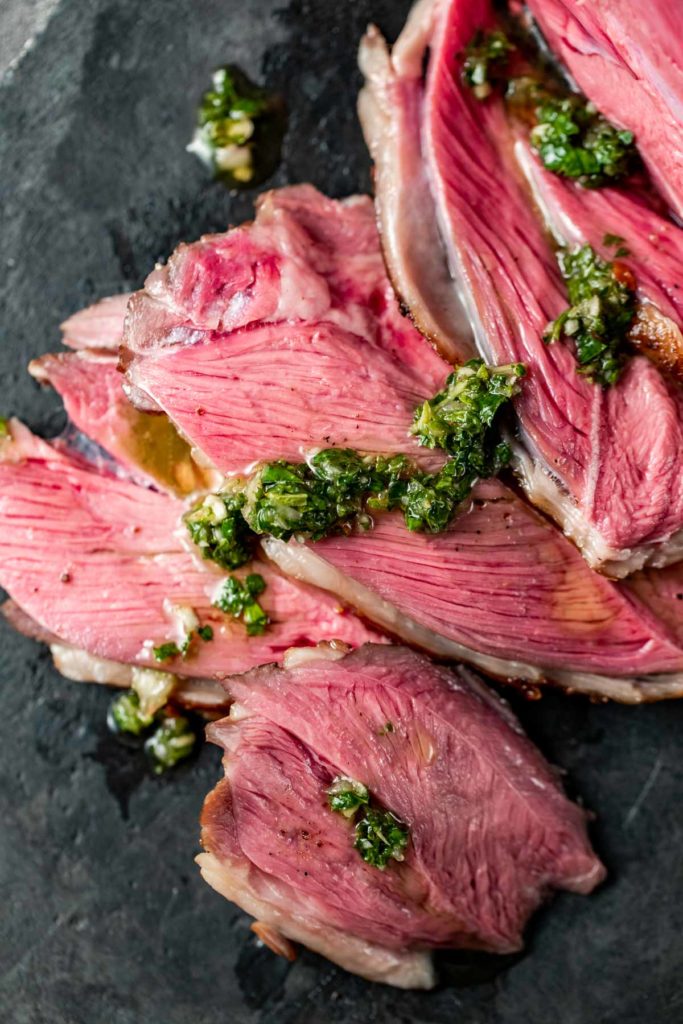 Overhead view of slices of leg of lamb topped with mint chimichurri.