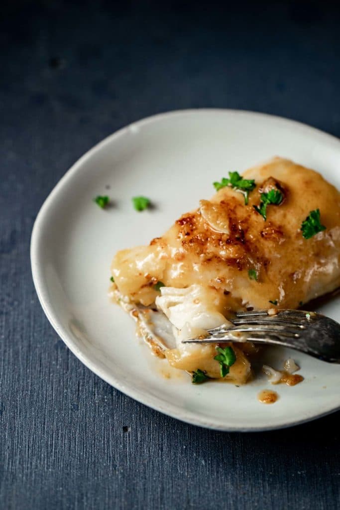 Sea bass on a white plate with a fork flaking a piece off.
