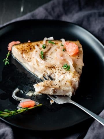Swordfish steak on a black plate with a fork removing a piece.