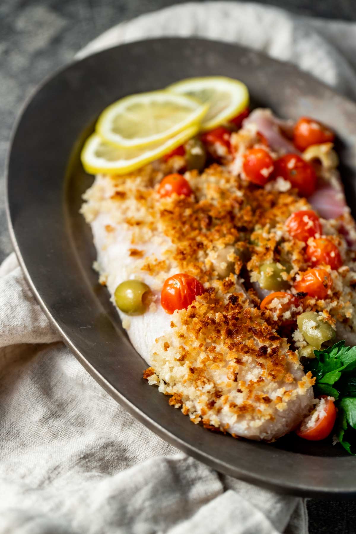 Side view of tilapia on a plate topped with crispy breadcrumbs.