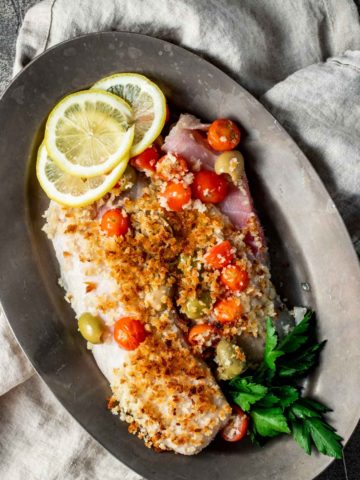 Overhead view of tilapia with tomatoes, olives and crispy breadcrumbs on top.