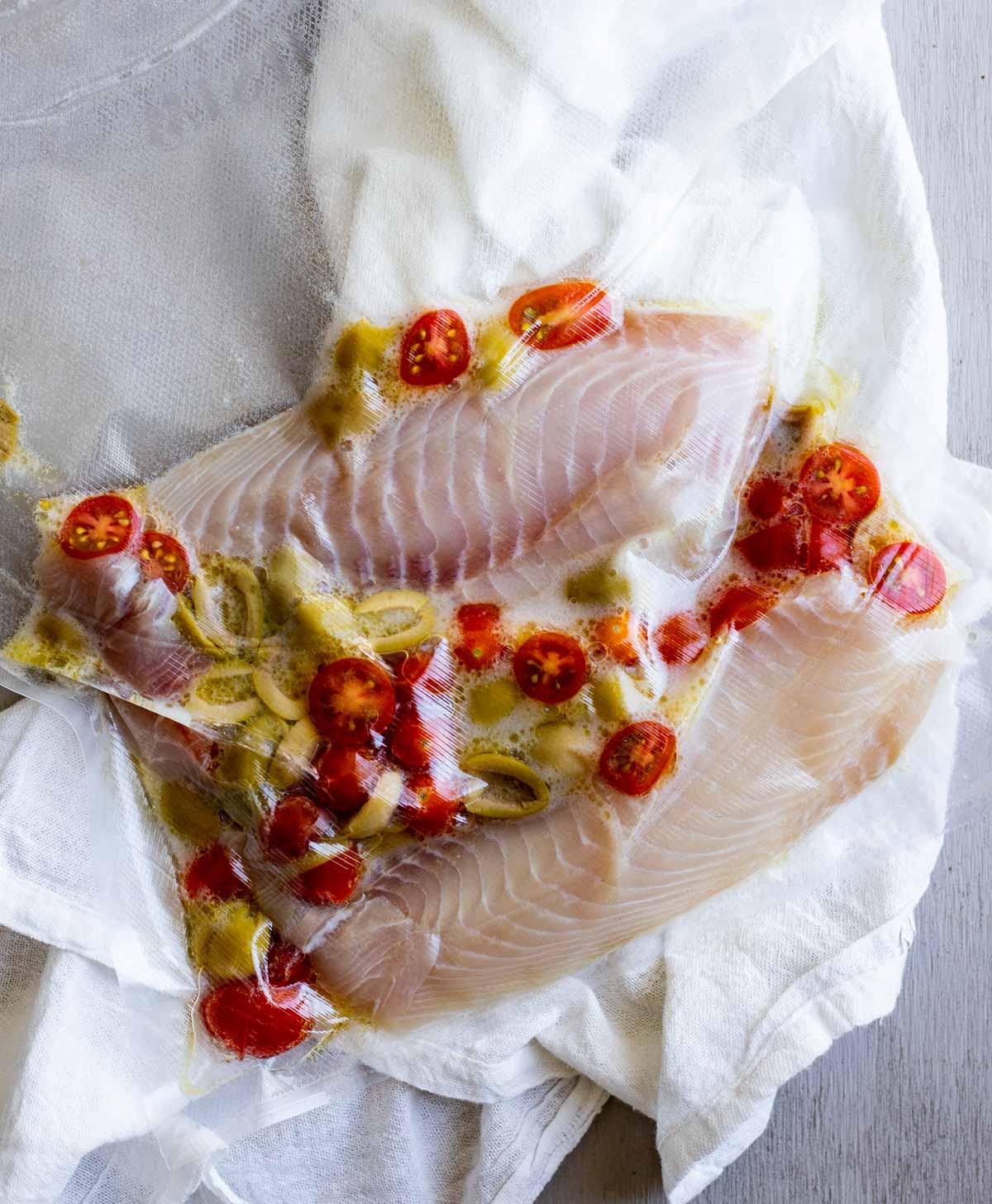 Tilapia fillets sealed in a bag with tomatoes, olives, wine and oil.