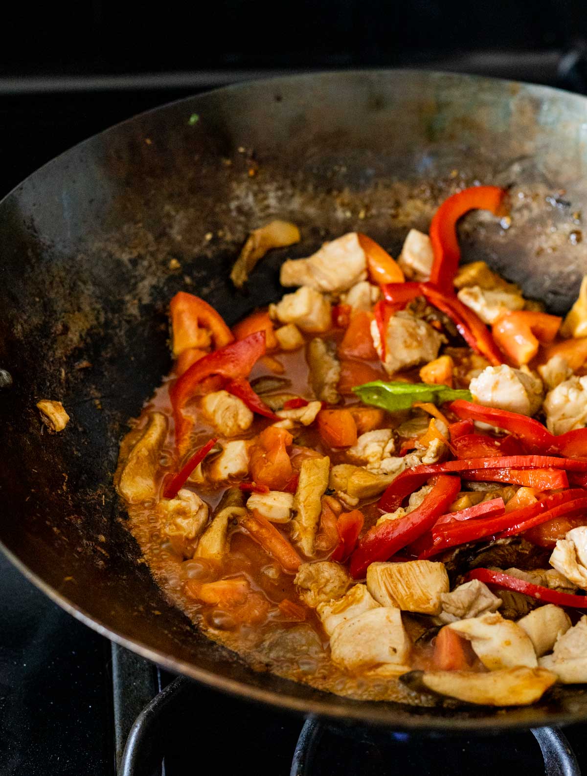 Vegetables and chicken cooking in tom yum sauce in a wok on the stovetop.