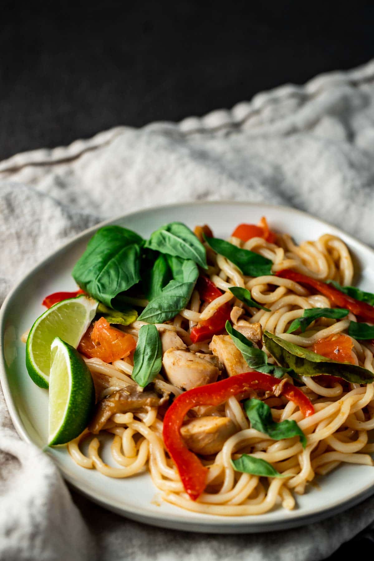 Tom yum noodles served on a plate with herbs and lime wedges.