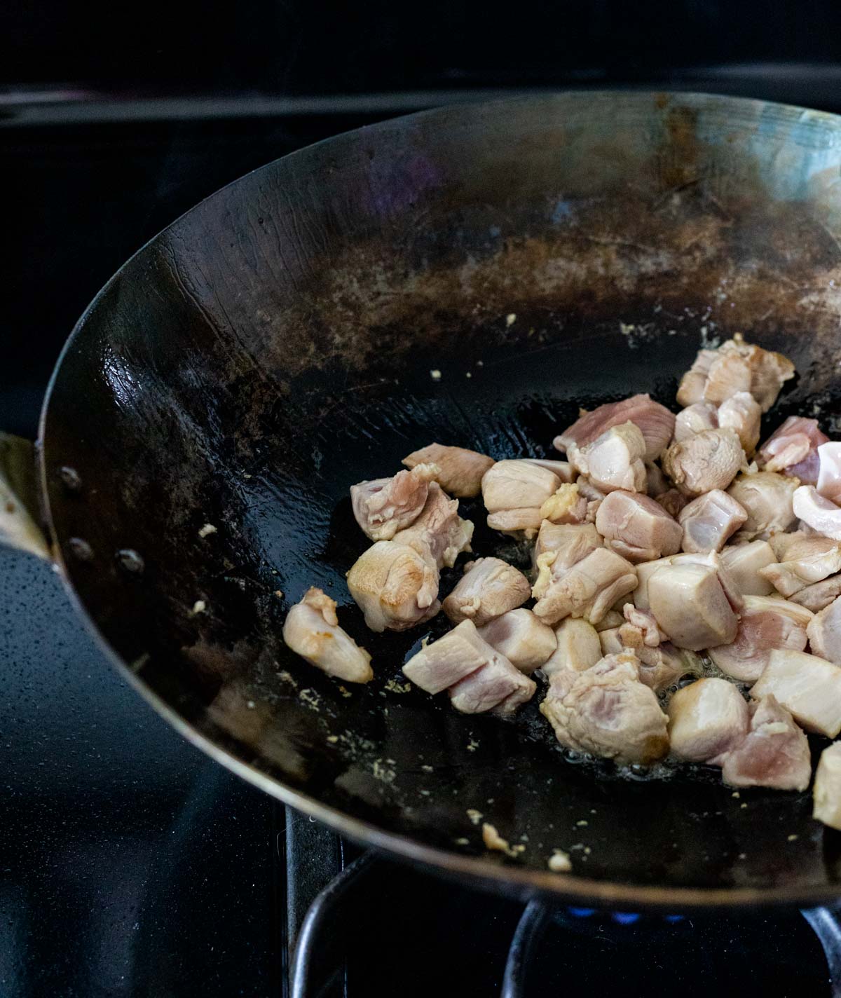 Chicken pieces cooking in a wok on the stovetop.