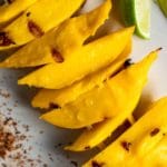 Close up view of grilled mango slices on a white plate.