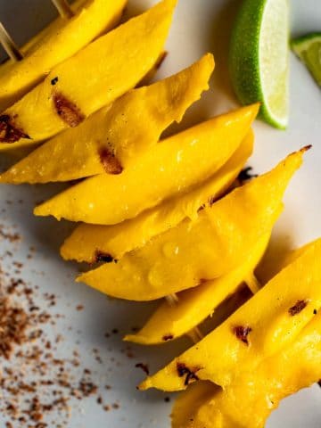 Close up view of grilled mango slices on a white plate.