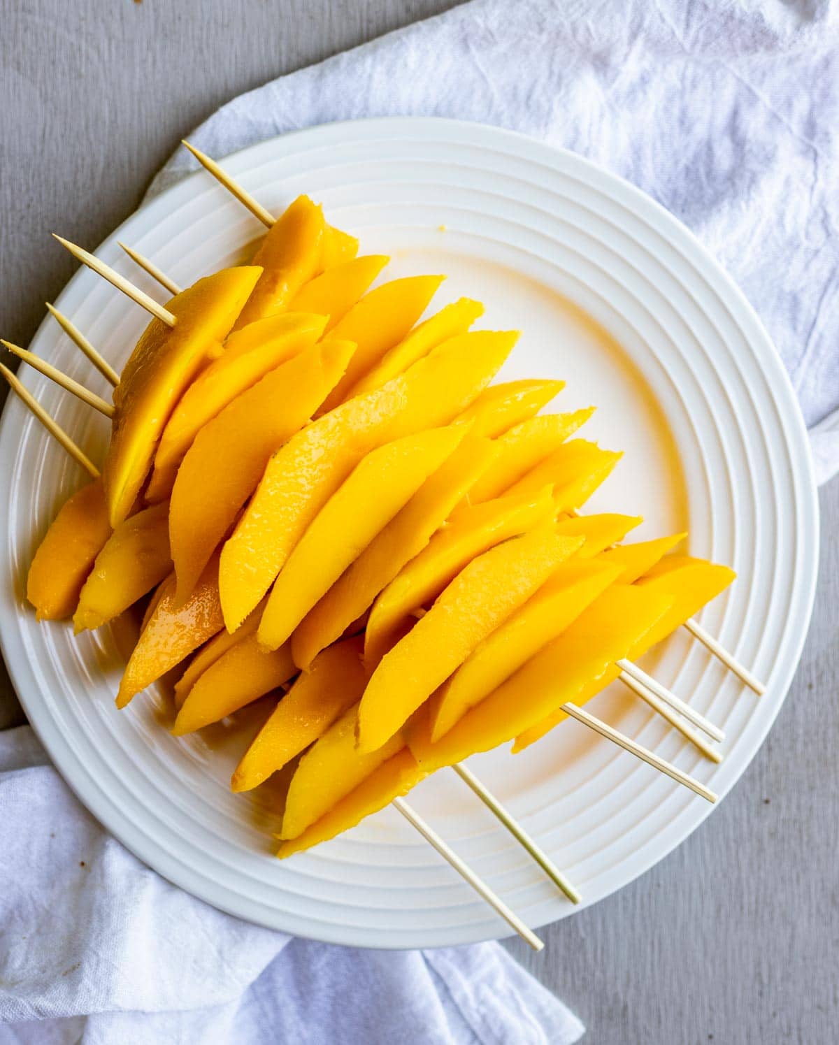 Sliced mangoes on skewers and piled on a white plate.