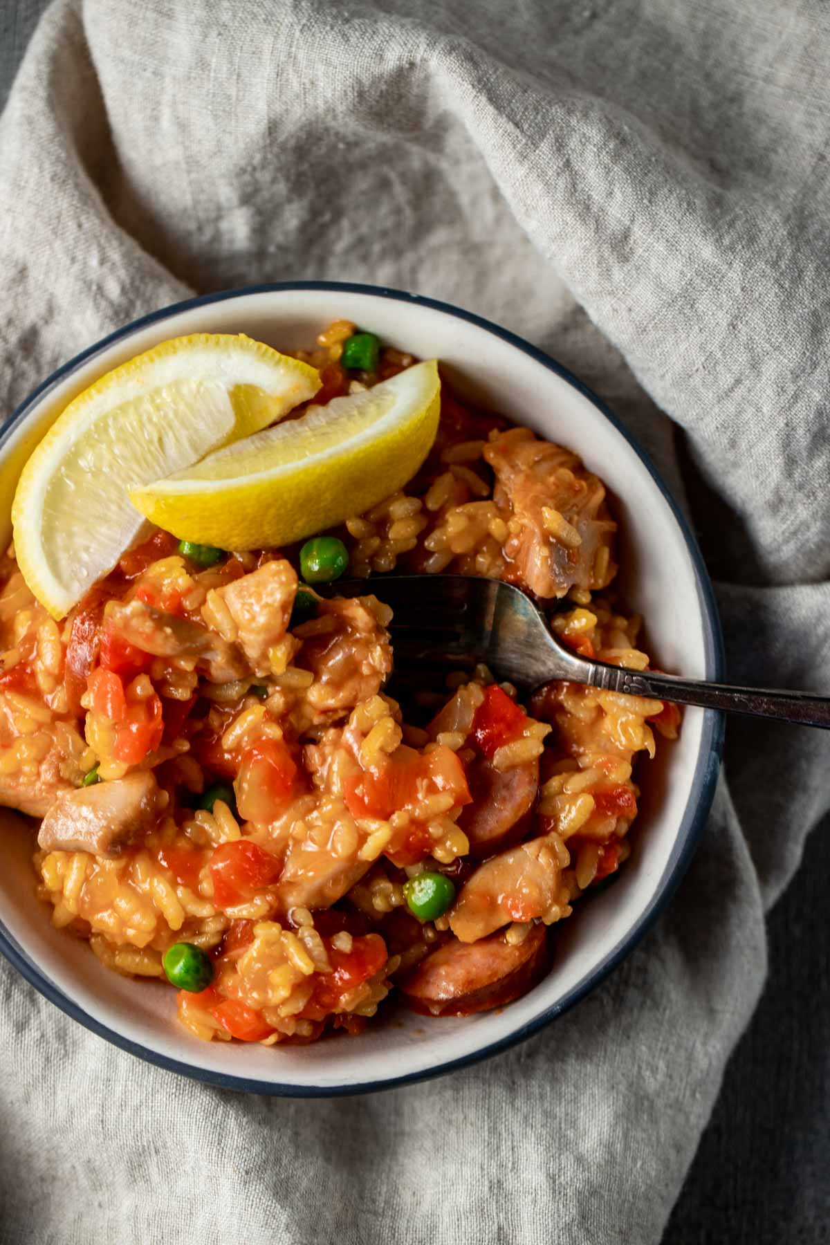 Overhead view of Instant Pot paella in a bowl with a fork inserted into it and lemon wedges on top.