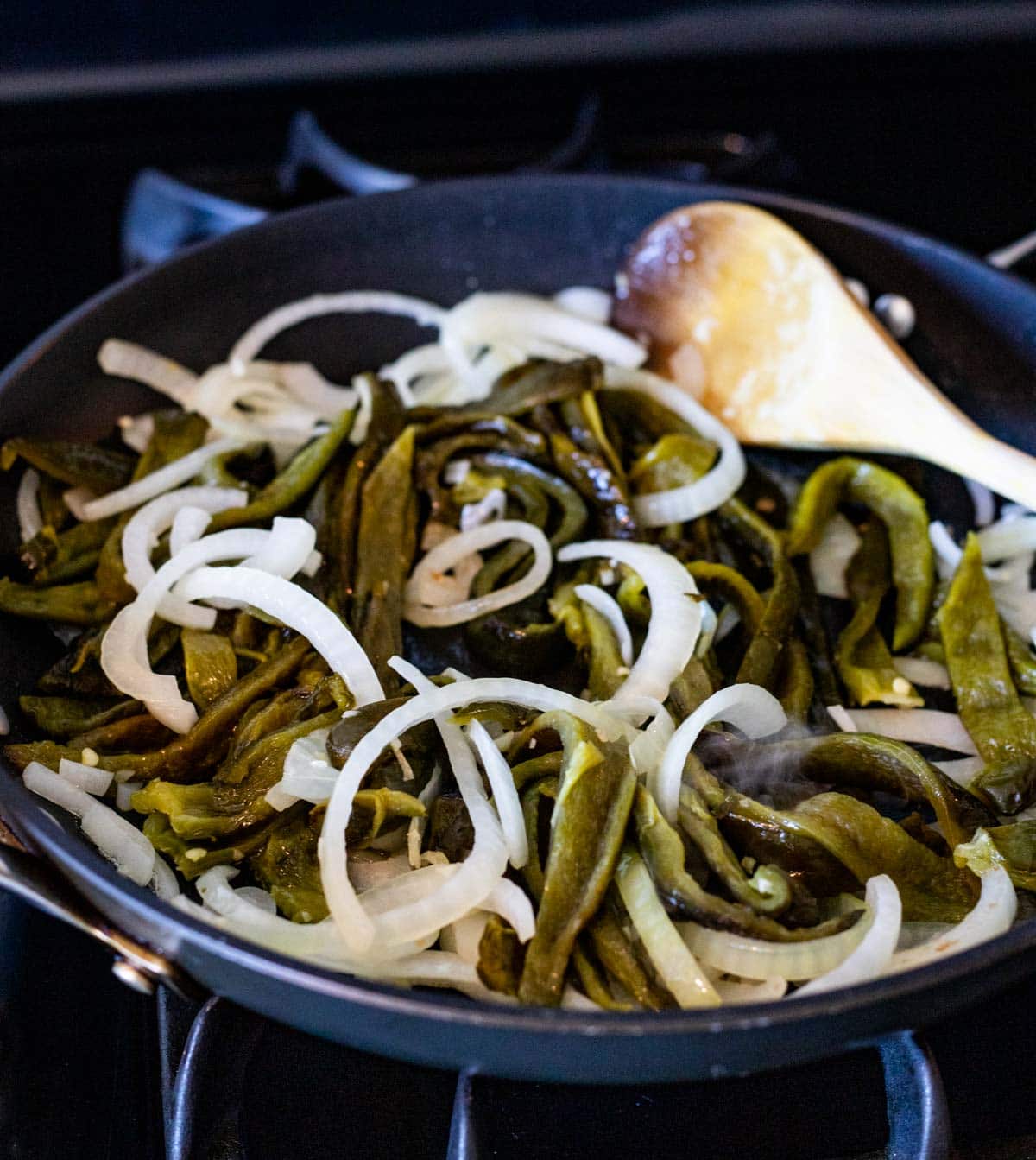 Sliced onions and strips of roasted poblano peppers cooking in a skillet.