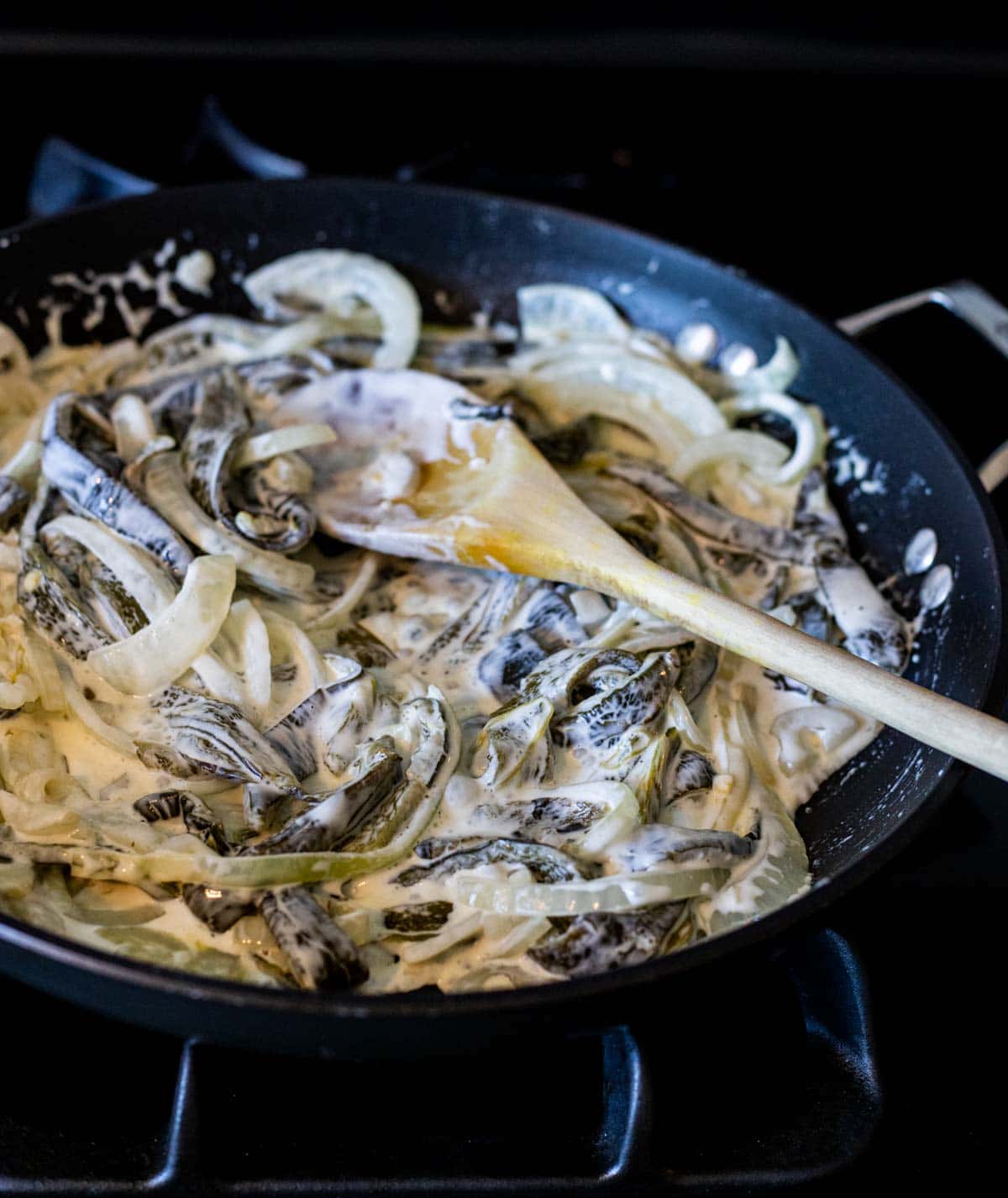 Roasted poblano peppers and onions in cream sauce cooking in a skillet.