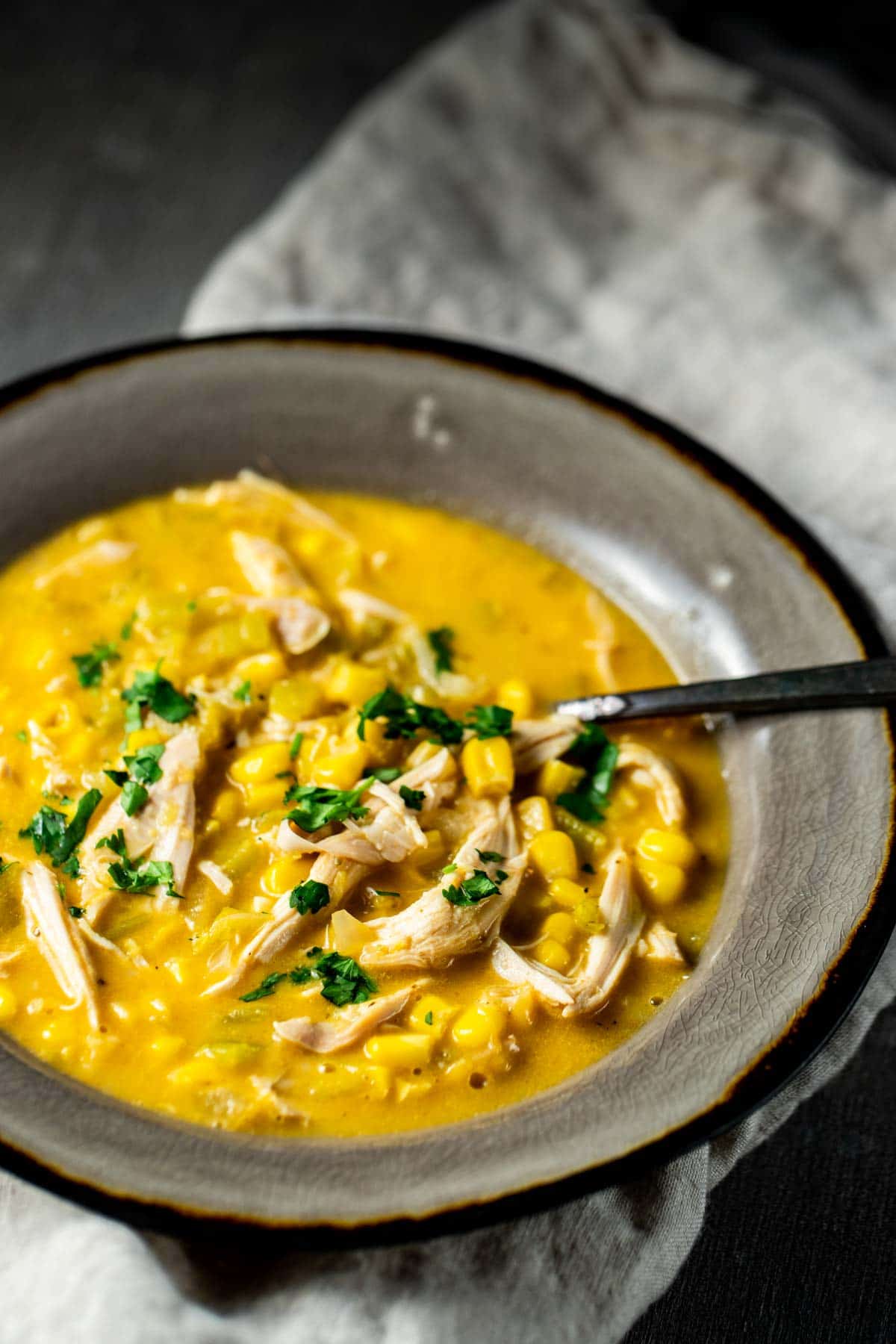 Sweet corn and chicken soup in a grey bowl with a spoon inserted into it.