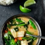 Overhead view of Thai green fish curry with a bowl of rice and lime wedges on the side.