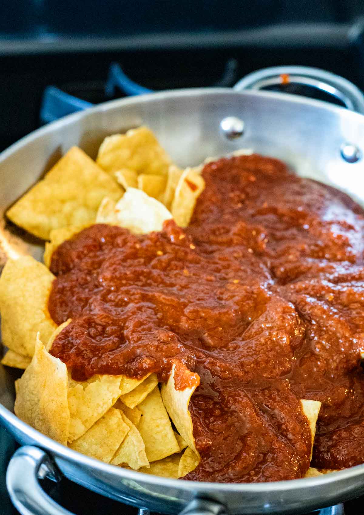 Tortilla chips in a skillet and topped with red sauce.
