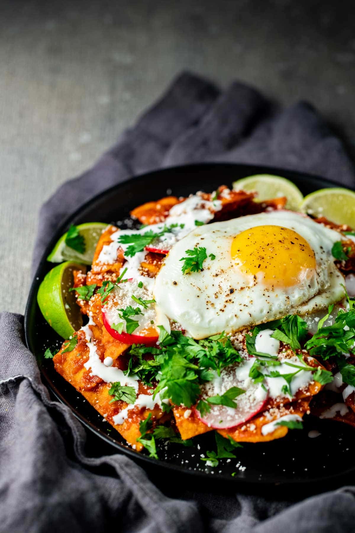 Chilaquiles rojos on a black plate and topped with a fried egg.