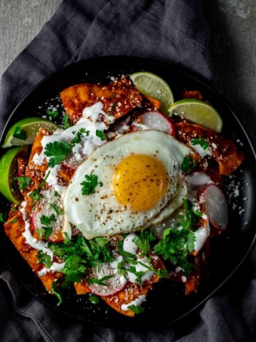 Overhead view of chilaquiles rojos topped with chopped herbs and a fried egg.