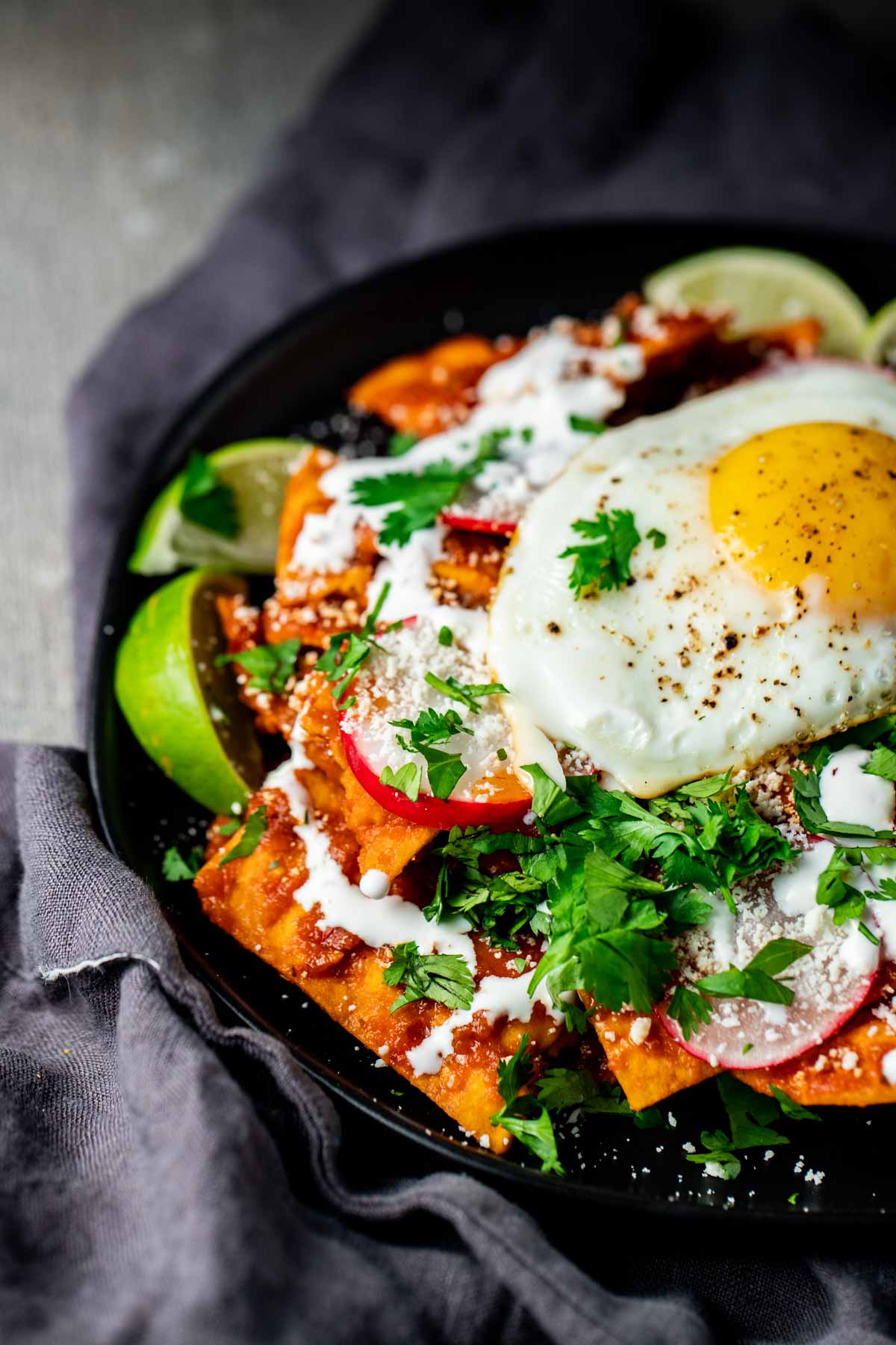 Close up view of red chilaquiles on a black plate.