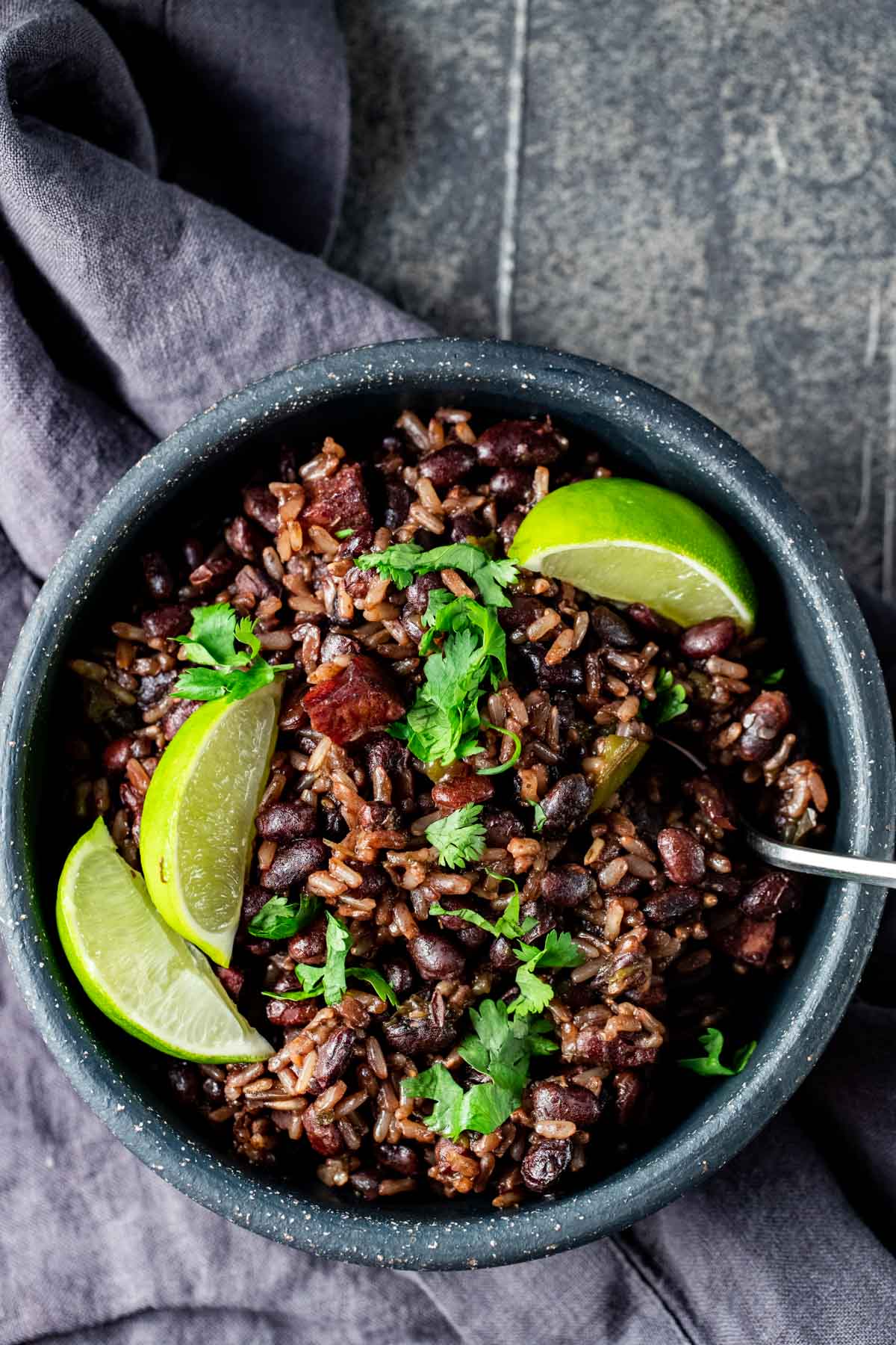 Overhead view of black beans and rice in a bowl with lime wedges on top.