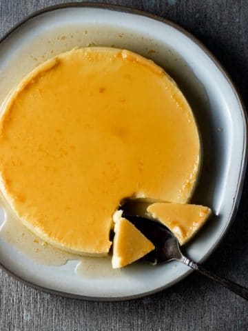 Overhead view of flan on a plate with some pieces removed with a serving utensil.